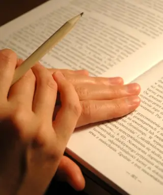 Photo a hand holding a pencil in front of a book signifying learning.